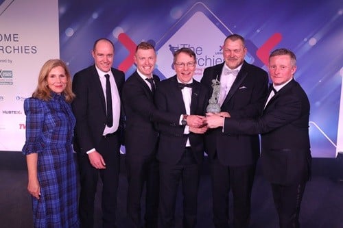 a group of five man and a blond woman on stage holding an award