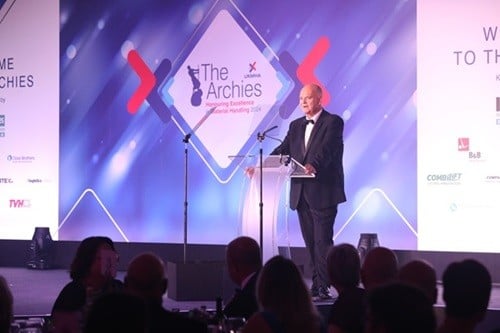 a middle aged man in dinner suit giving speach on stage